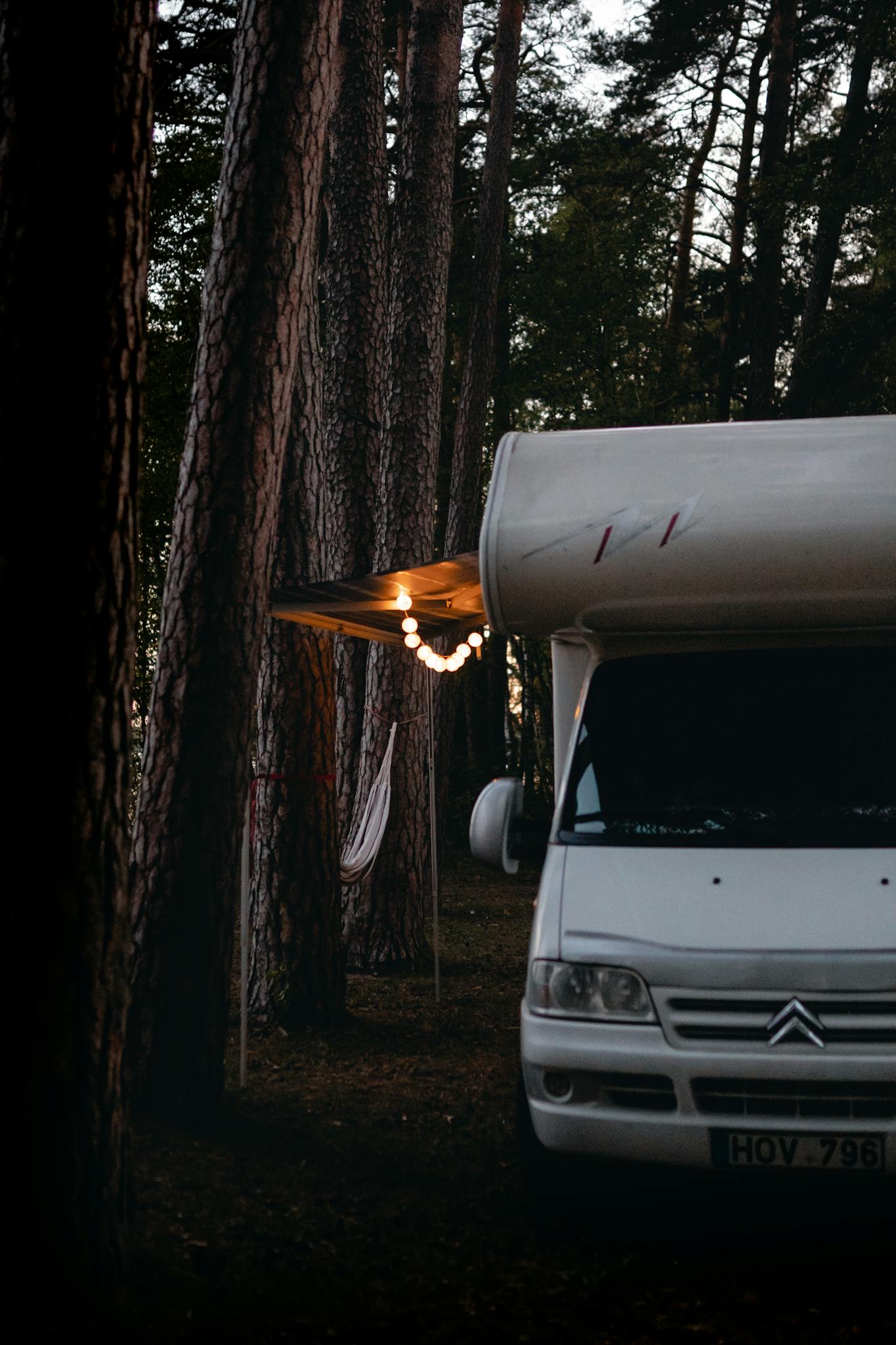 Camper van parked in a serene forest with warm lights, creating a cozy ambiance at twilight.
