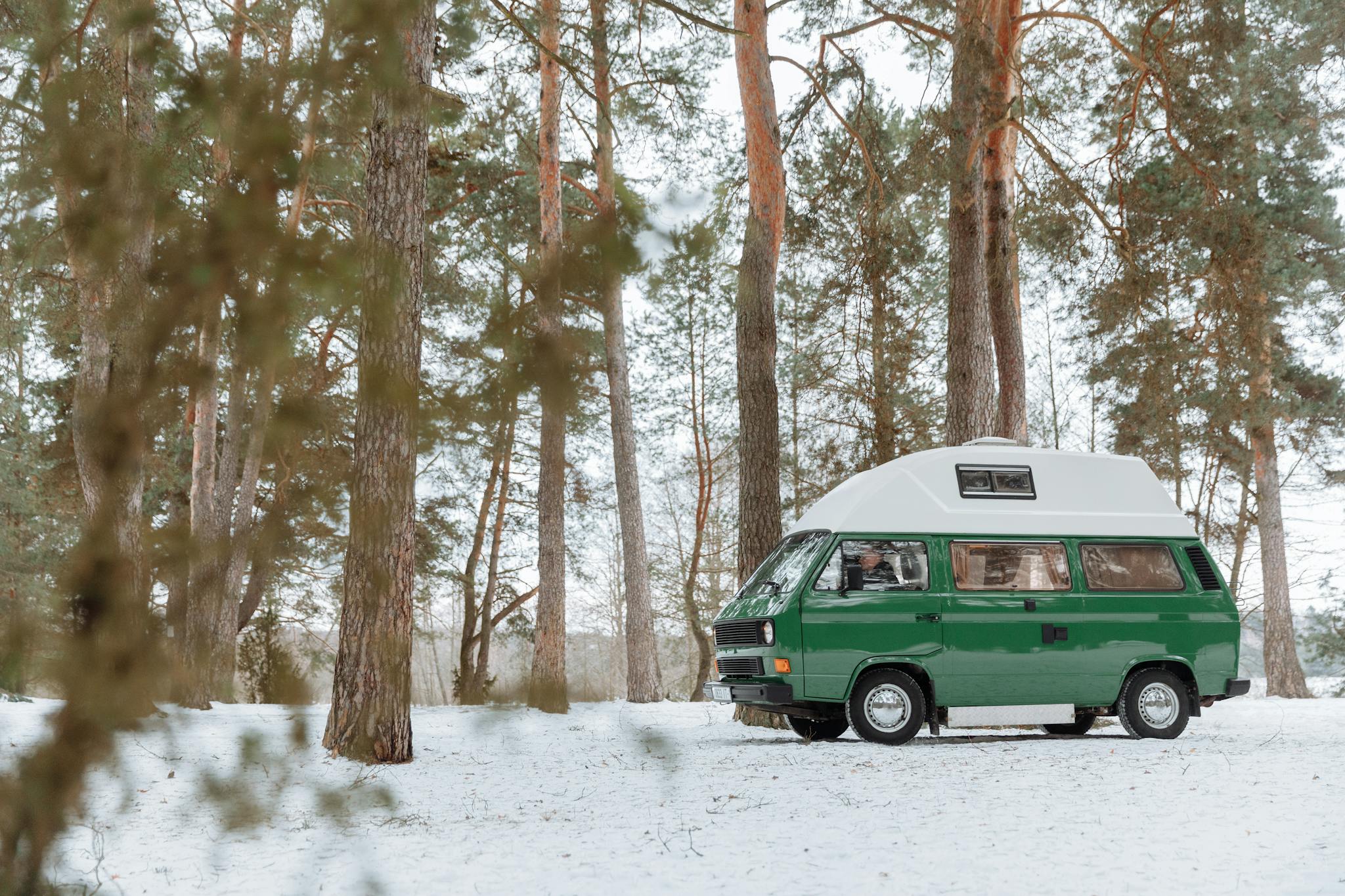 Explore the tranquil beauty of winter with a classic green camper van parked in a snowy forest.