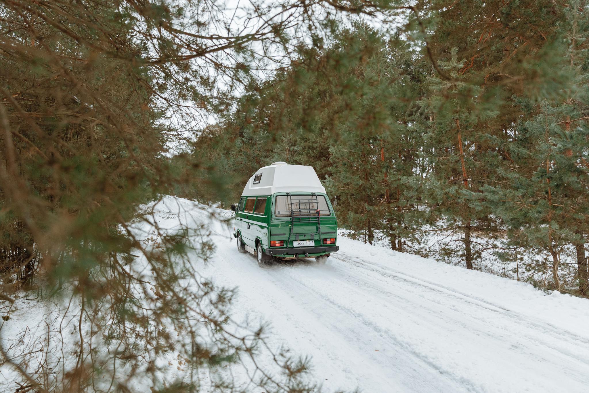 Green camper van driving on a snowy forest road during winter, capturing the spirit of adventure.
